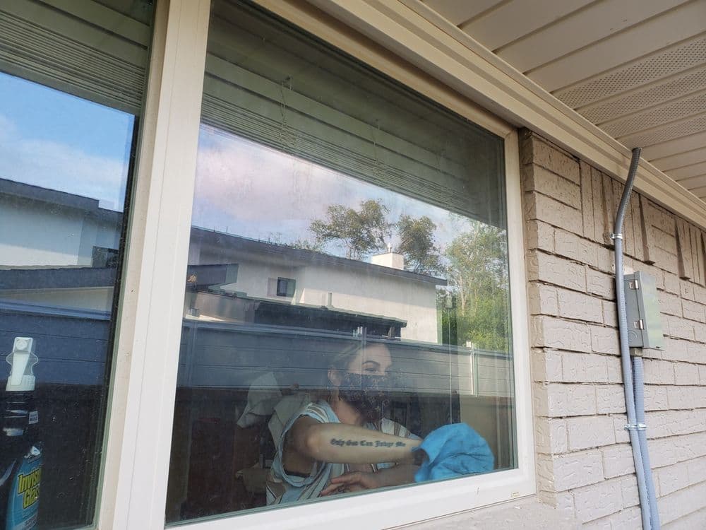 Person wearing a mask reflected in a window, surrounded by a residential setting.