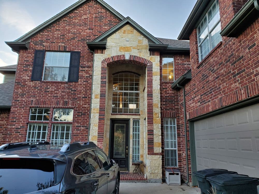 Brick house exterior with stone accents, large arched entryway, and parked SUV in driveway.